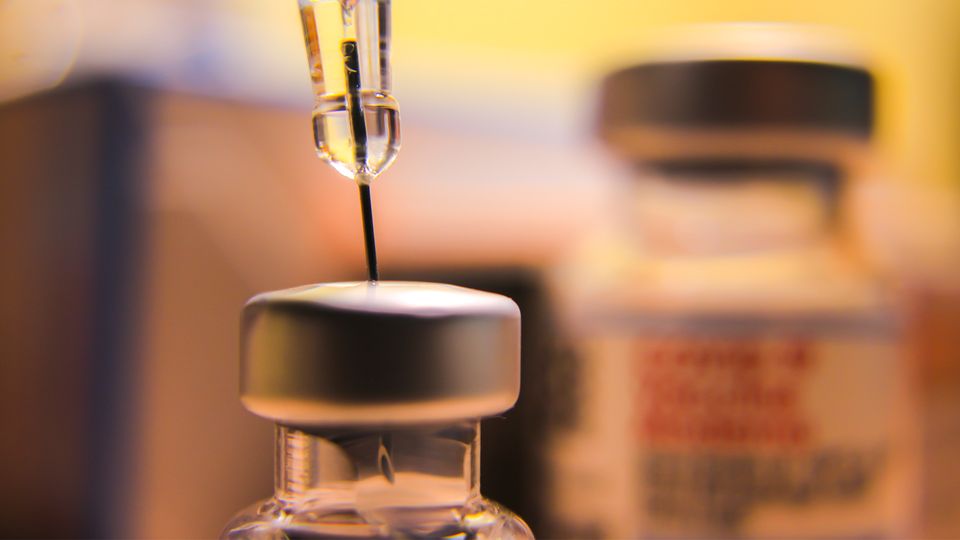 A close-up of a syringe drawing liquid from a vaccine vial.