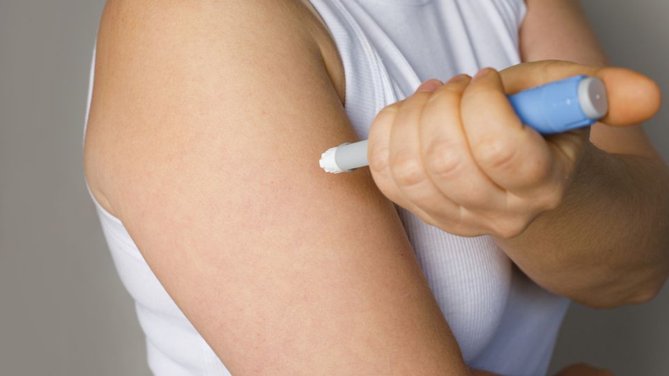 Someone injecting their right arm with an EpiPen, or a prop resembling an EpiPen.