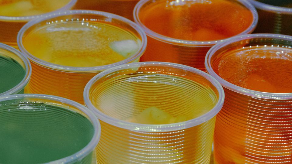 Green, yellow and orange drinks in plastic cups.