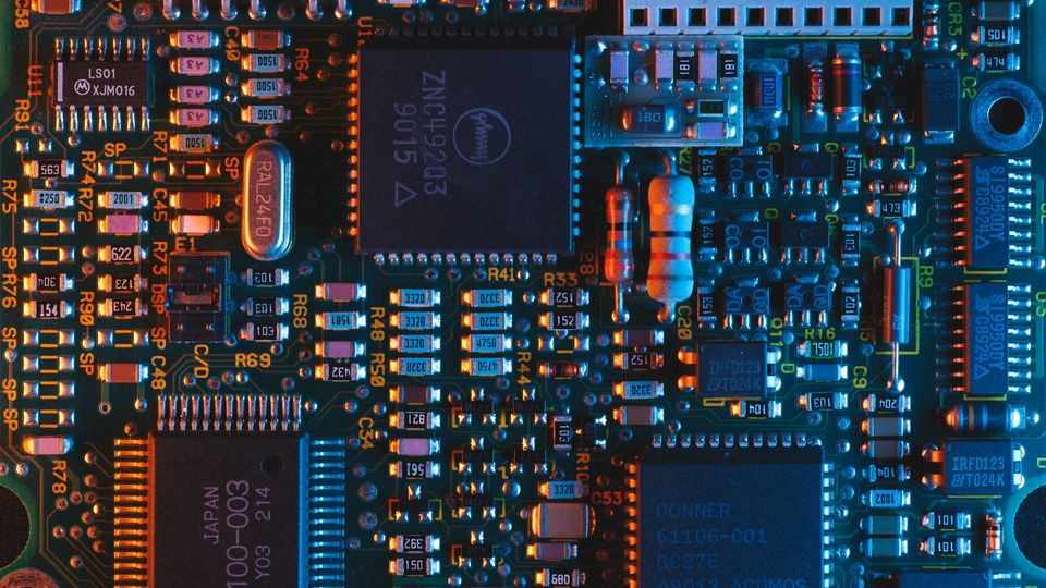 A top-down photograph of a computer motherboard, lit with orange and blue lighting.