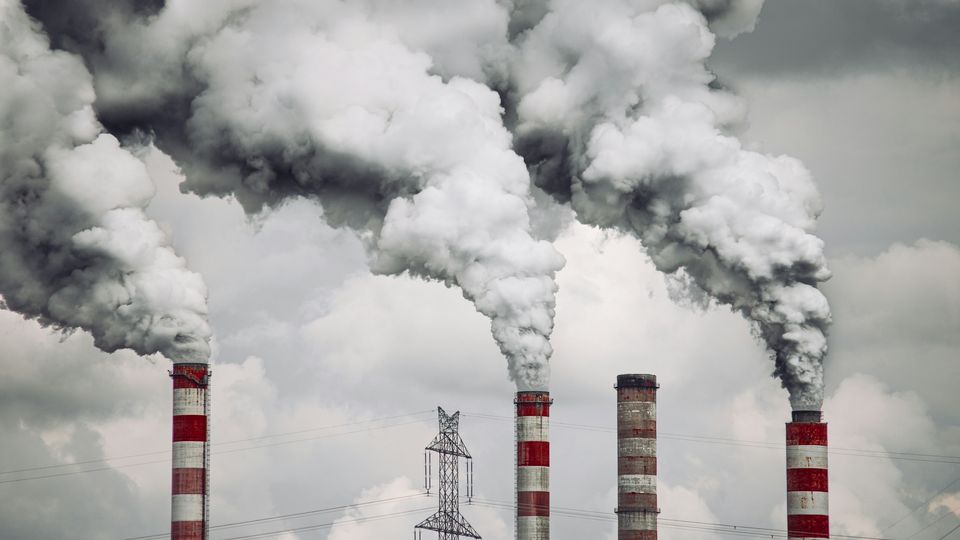 Red and white industrial chimney's emitting grey smoke above a skyline.