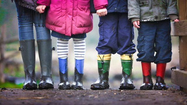 The lower half of four people, three clearly children. All wearing Wellington boots and dressed for the rain.