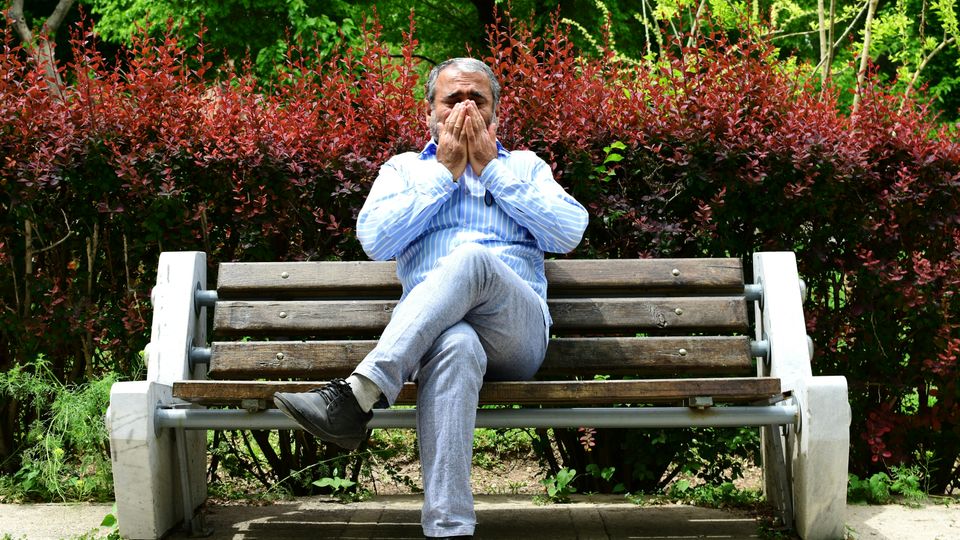 A man sitting on a park bench, sneezing.