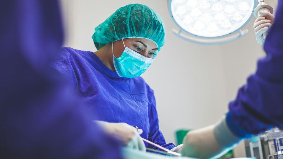 A female surgeon in a blue surgical robe and face mask.