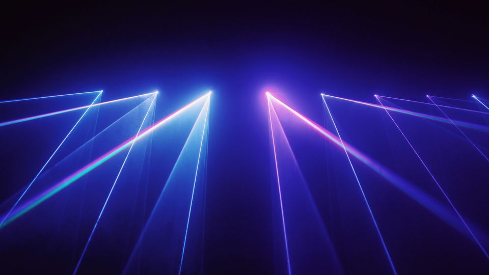 Blue and pink laser lights shining through the fog from the top of a stage.