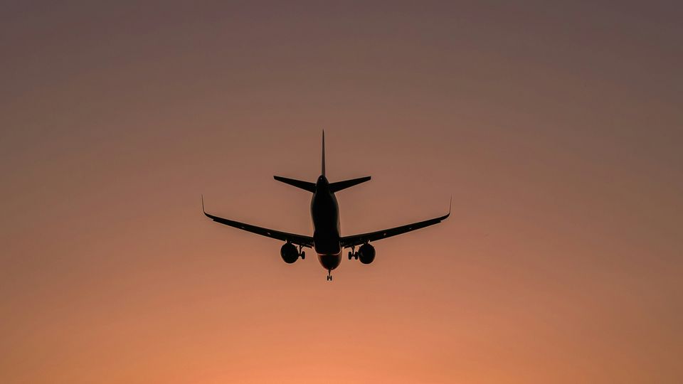 A silhouette of a plane descending against an orange sky.