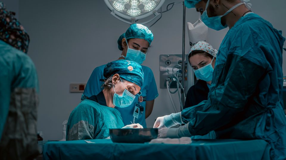 A female surgeon in a surgery room, surrounded by her surgical team.