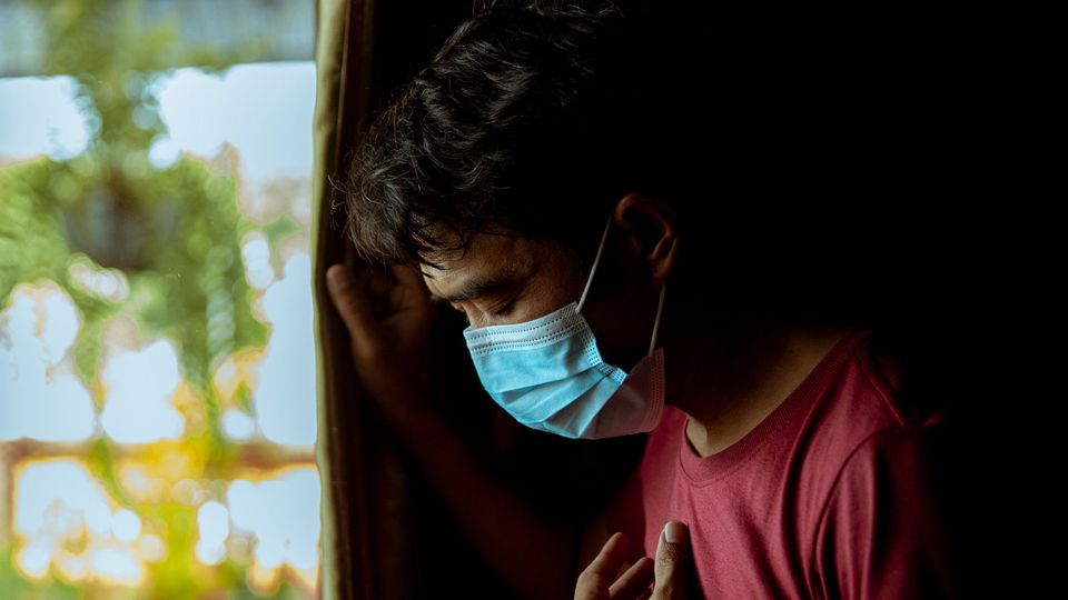 A man wearing a facemask puts his hand to his chest, looking ill.