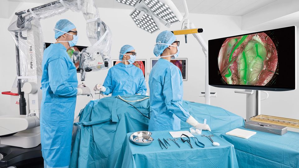 Surgeons using a hybrid surgical microscope with real-time imaging during an operating procedure.