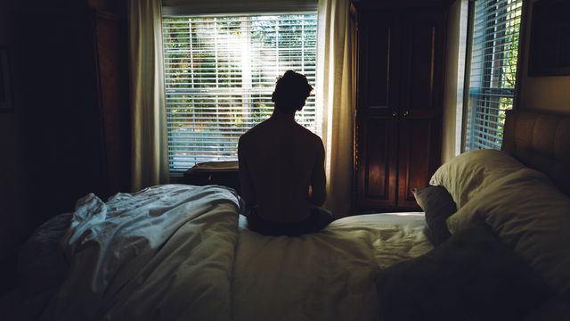 Silhouetted person sitting alone on a bed in a dimly lit room, reflecting emotional grief. 