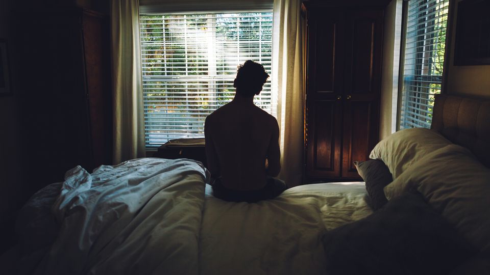 Silhouetted person sitting alone on a bed in a dimly lit room, reflecting emotional grief.