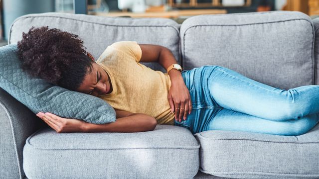 Woman lying on a couch in discomfort, holding her stomach, possibly experiencing PMDD symptoms.