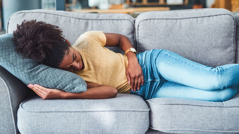 Woman lying on a couch in discomfort, holding her stomach, possibly experiencing PMDD symptoms.