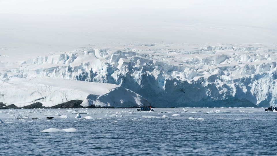 The ice cliffs of Antarctica, small boat visible in the sea.