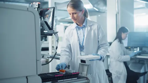 Female scientist placing sample tubes into an automated lab analyzer in a modern laboratory.