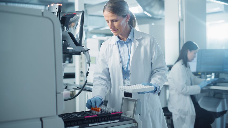 Female scientist placing sample tubes into an automated lab analyzer in a modern laboratory.
