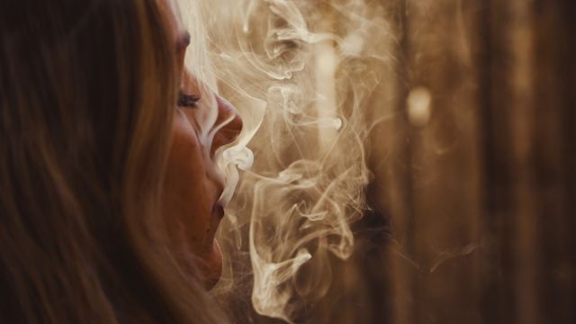 Woman exhaling cigarette smoke, illustrating nicotine use and inhalation.