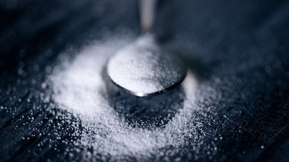 A teaspoon of white powder sweetener lying on a dark gray surface.