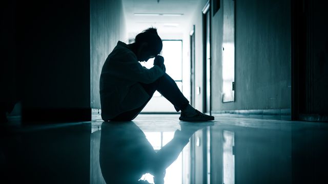 Silhouetted person sitting alone in a dim hallway, head down, reflecting symptoms of depression.