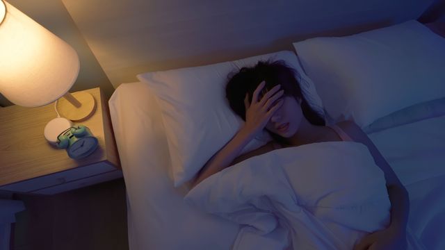 Woman lying in bed at night with hand on forehead, showing signs of insomnia and restlessness. 
