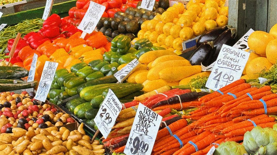 A market stall full of different vegetables, carrots, courgettes, aubergines, etc. Prices given on paper.