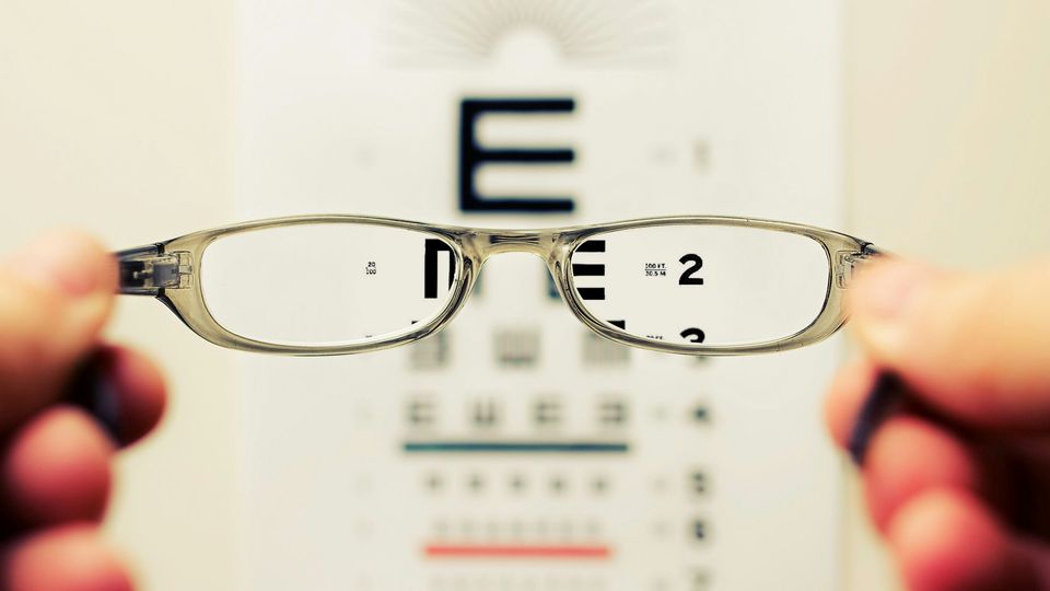 A POV photograph looking through a pair of glasses towards a standard eye exam letter chart.