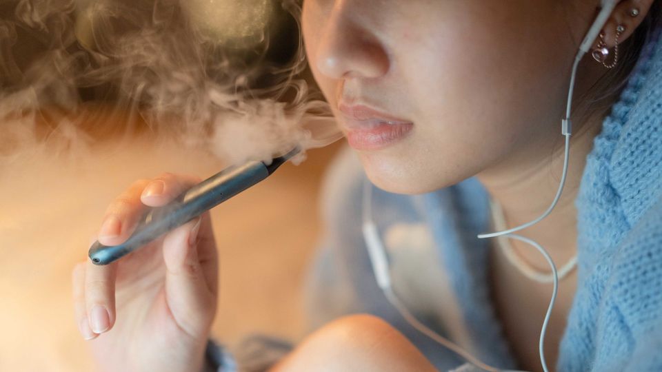 Close-up of a woman listening to music whilst vaping.