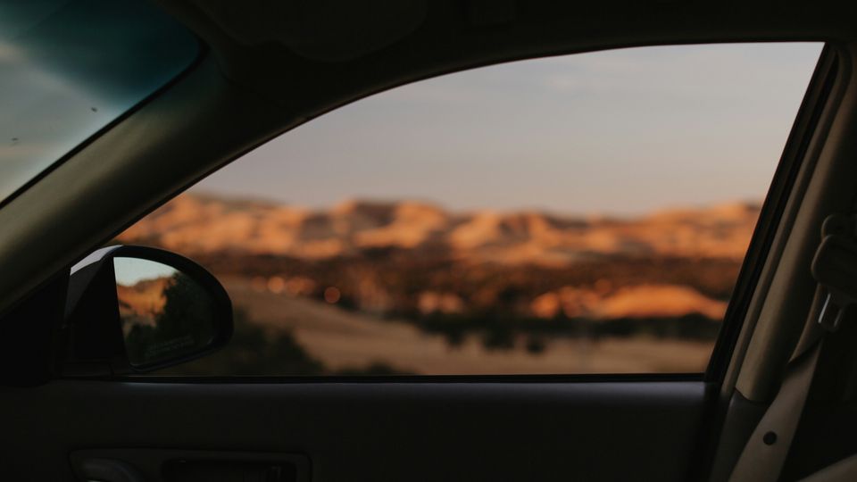 The view from inside a tinted car window, as it travels through an orange, desert-like landscape.