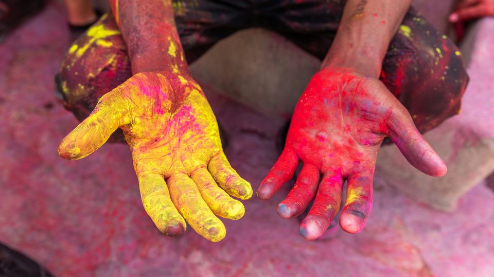 A person holds out their hands covered in yellow and red pigment, during a celebration for Holi.