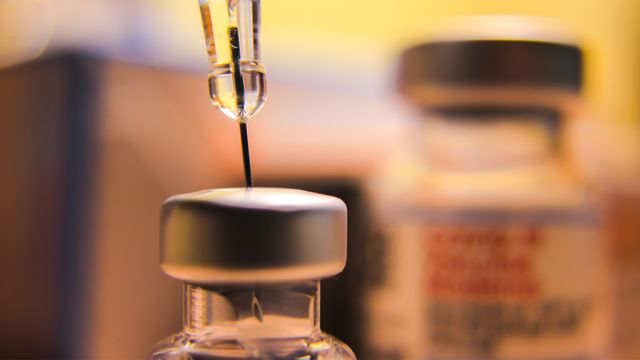 A close-up of a syringe drawing liquid from a vial containing COVID-19 vaccine.