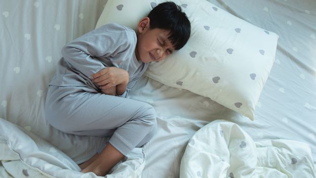 Young boy in pajamas lying in bed clutching his stomach in visible pain. 