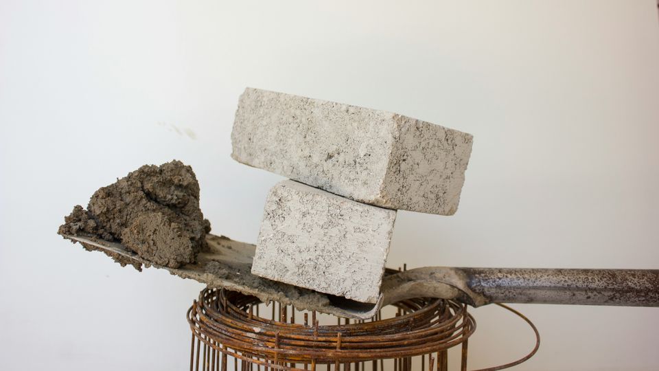 Two concrete blocks balancing on top of a shovel with a scoop of concrete on its end.