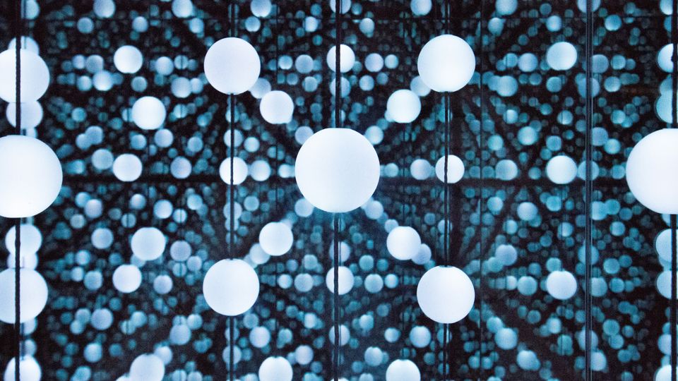 A collection of blue balls lit up in a mirror room so it looks like an endless expanse of multi-layered material.