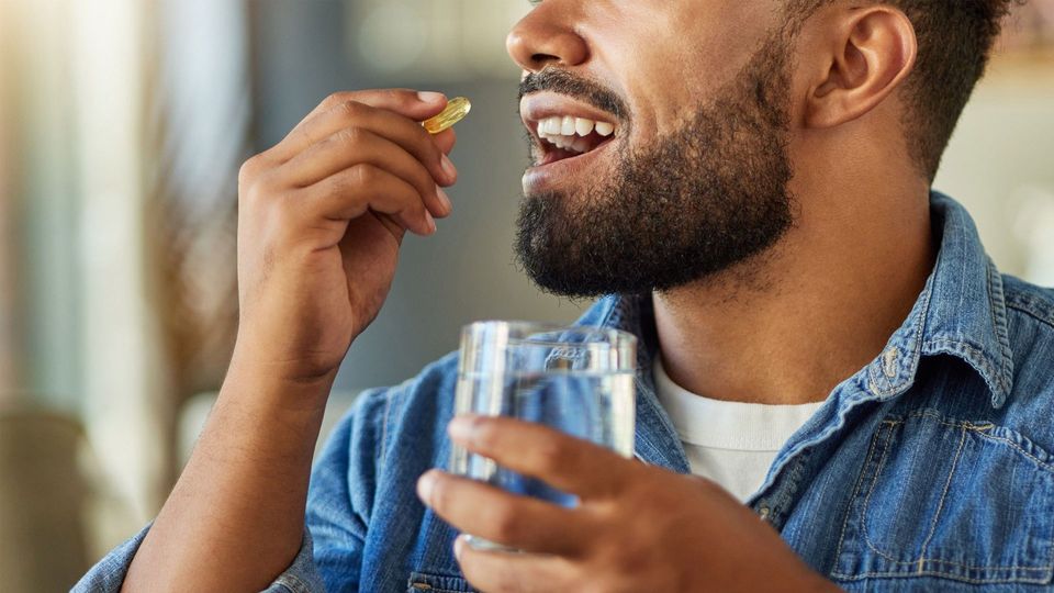 Man taking a probiotic capsule with a glass of water in hand.