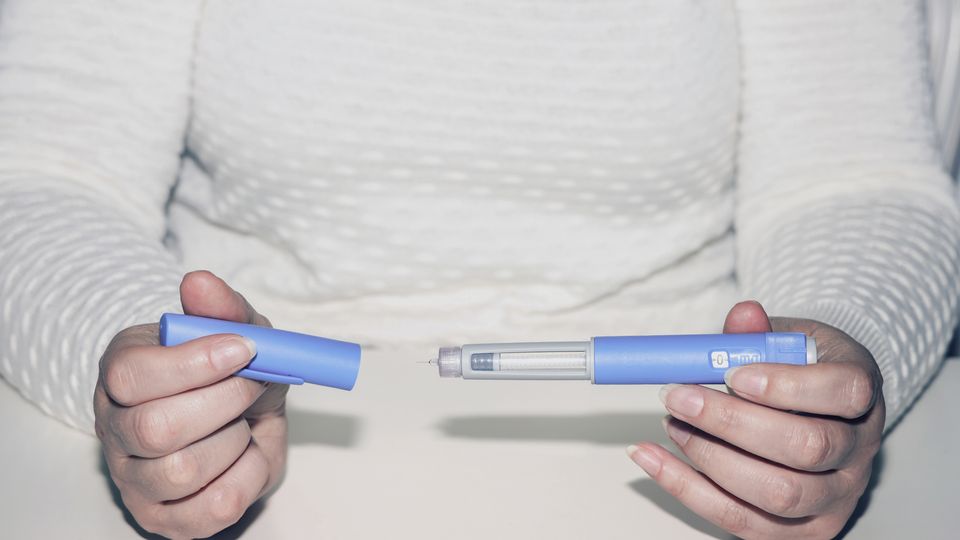 A person holding a drug pen containing a GLP-1 drug.