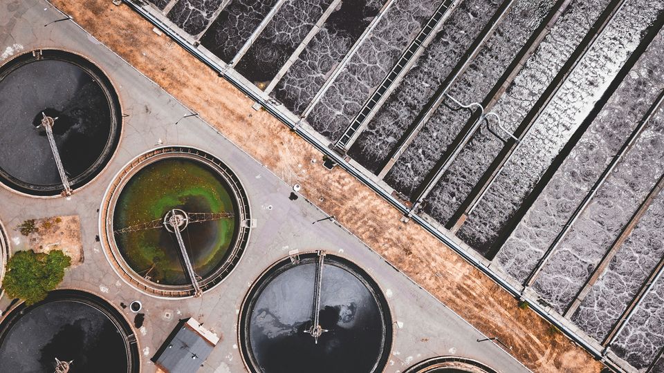 An aerial view of a water treatment facility, featuring round water tankers and straight waterways.