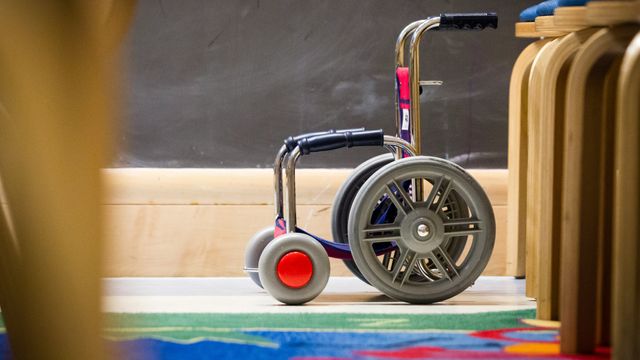 Pediatric wheelchair beside chairs in a classroom, symbolizing mobility challenges in children with alternating hemiplegia of childhood. 