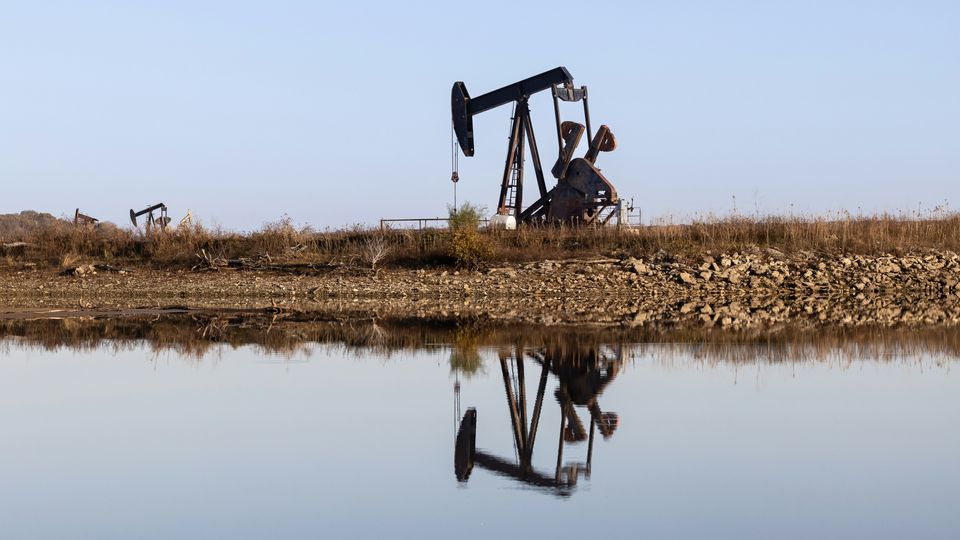 An oil pump in a field, reflected in a nearby body of water