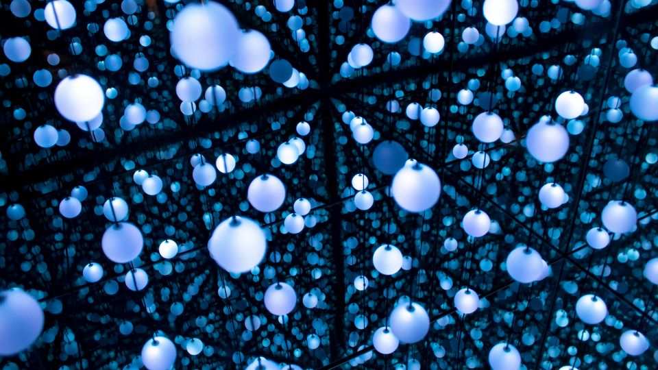 A photo of an art exhibit, in which blue-lit balls are hung around a mirrored room, appearing to stretch out infinitely.