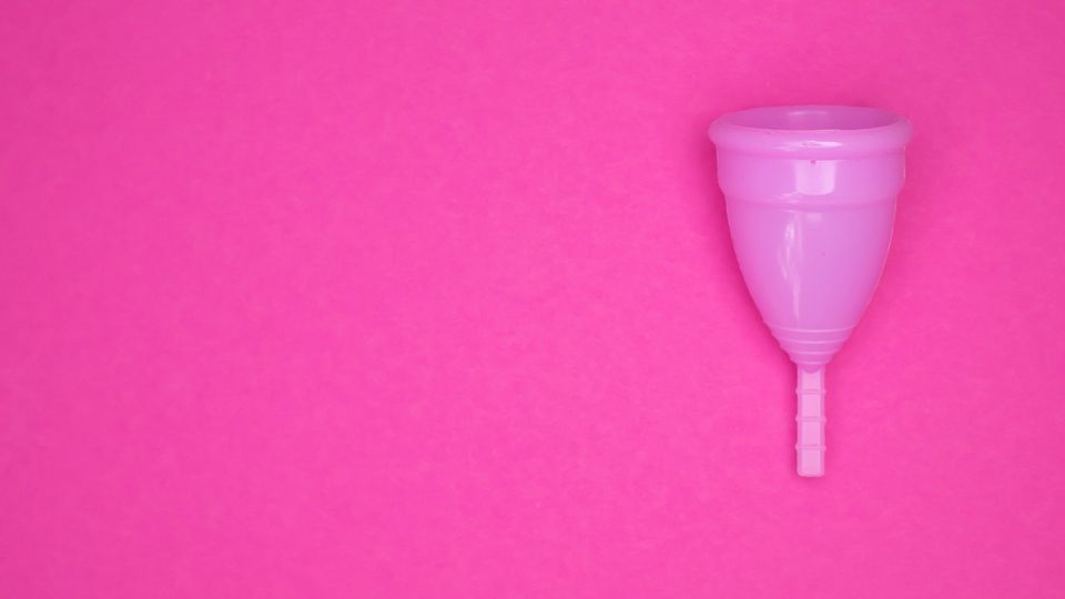 Pink menstrual cup on bright pink background representing reusable menstrual products.