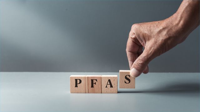 A hand lining up a row of small wooden blocks that spell out "PFAS"