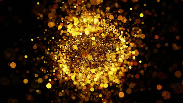A slightly blurred image of a large amount of gold glitter, falling away from the camera onto a black surface. 