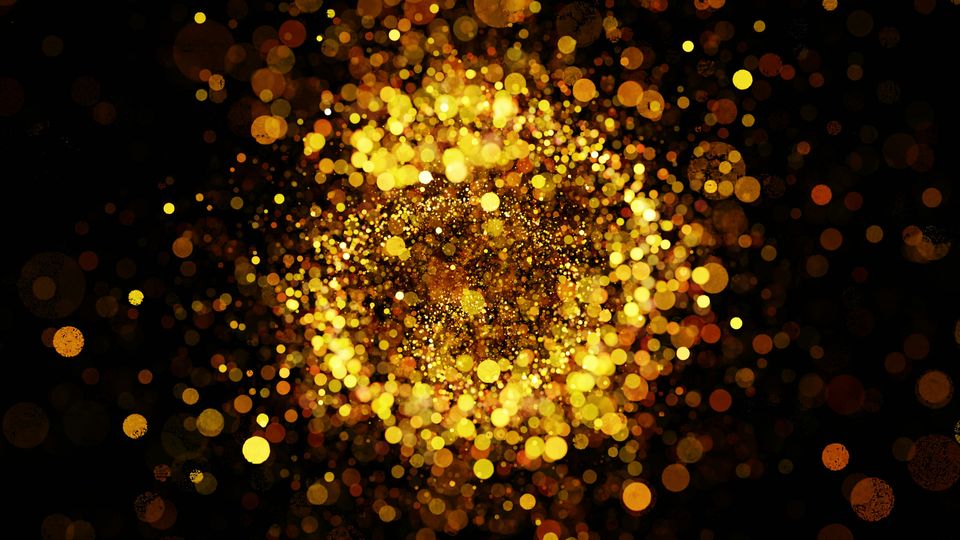 A slightly blurred image of a large amount of gold glitter, falling away from the camera onto a black surface.