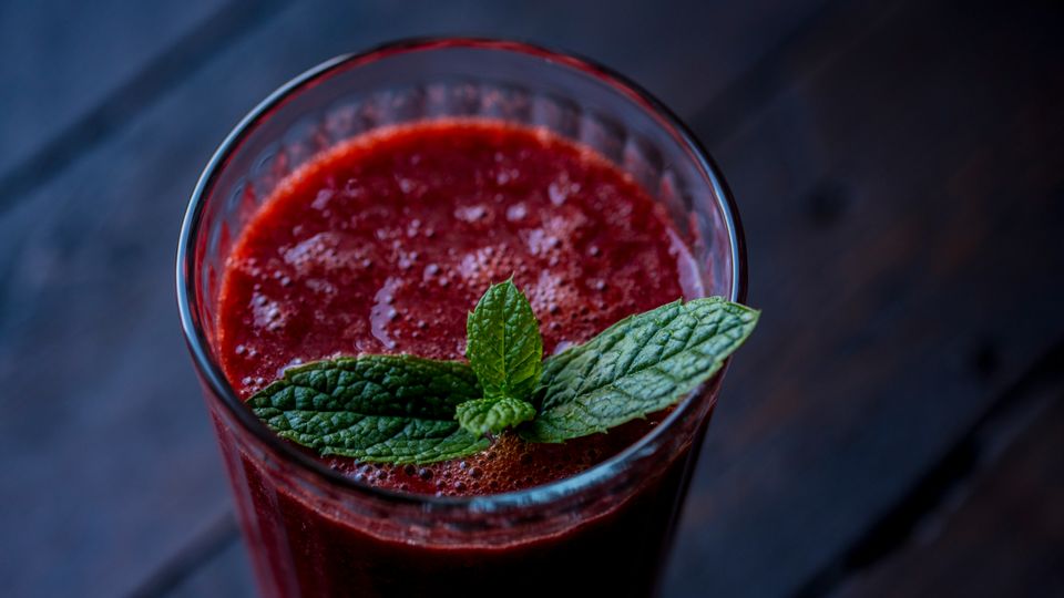 A glass of red smoothie, decorated with leaves.