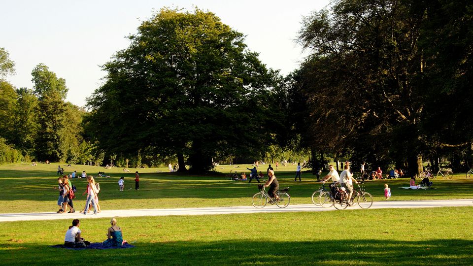 People walking and cycling through a green public park.