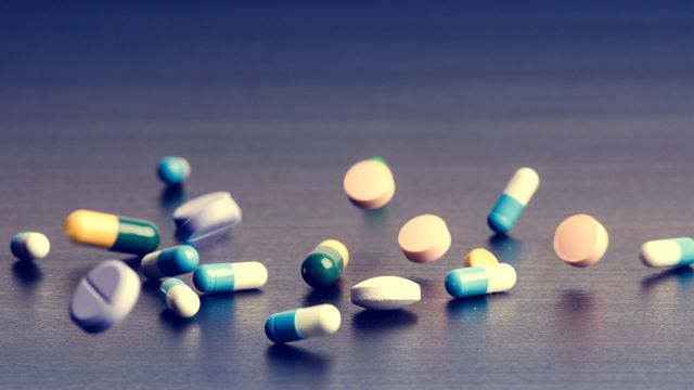 Various different drug capsules falling across a table top.