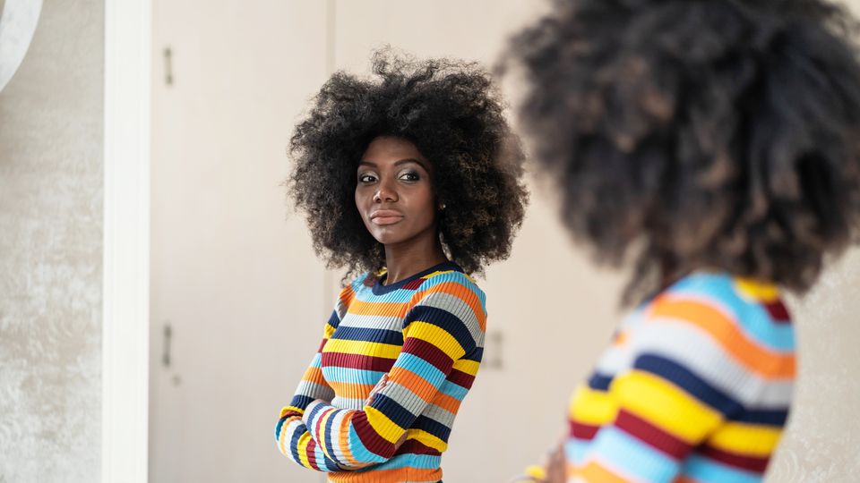 Woman in colorful striped sweater looking at her reflection in a mirror.