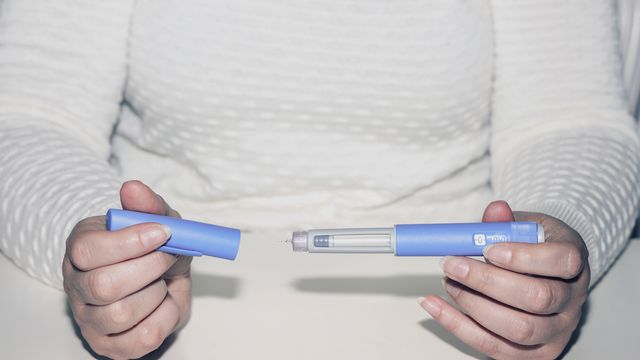 A pair of hands holding a drug pen containing GLP-1 drugs for treating obesity.