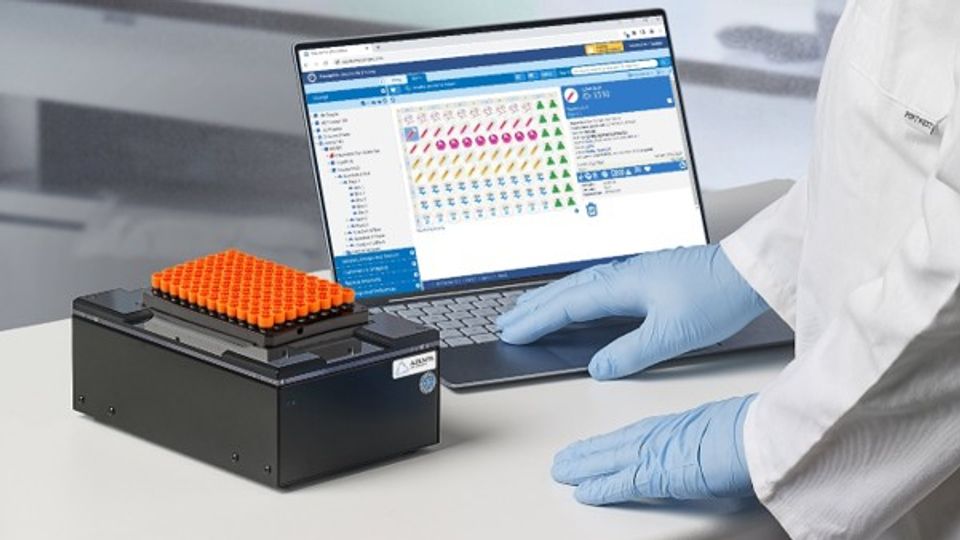 Scientist using a web-based sample management inventory system with lab tubes and laptop interface.