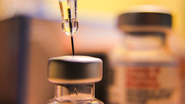 A close-up of a syringe drawing liquid from a vaccine vial.